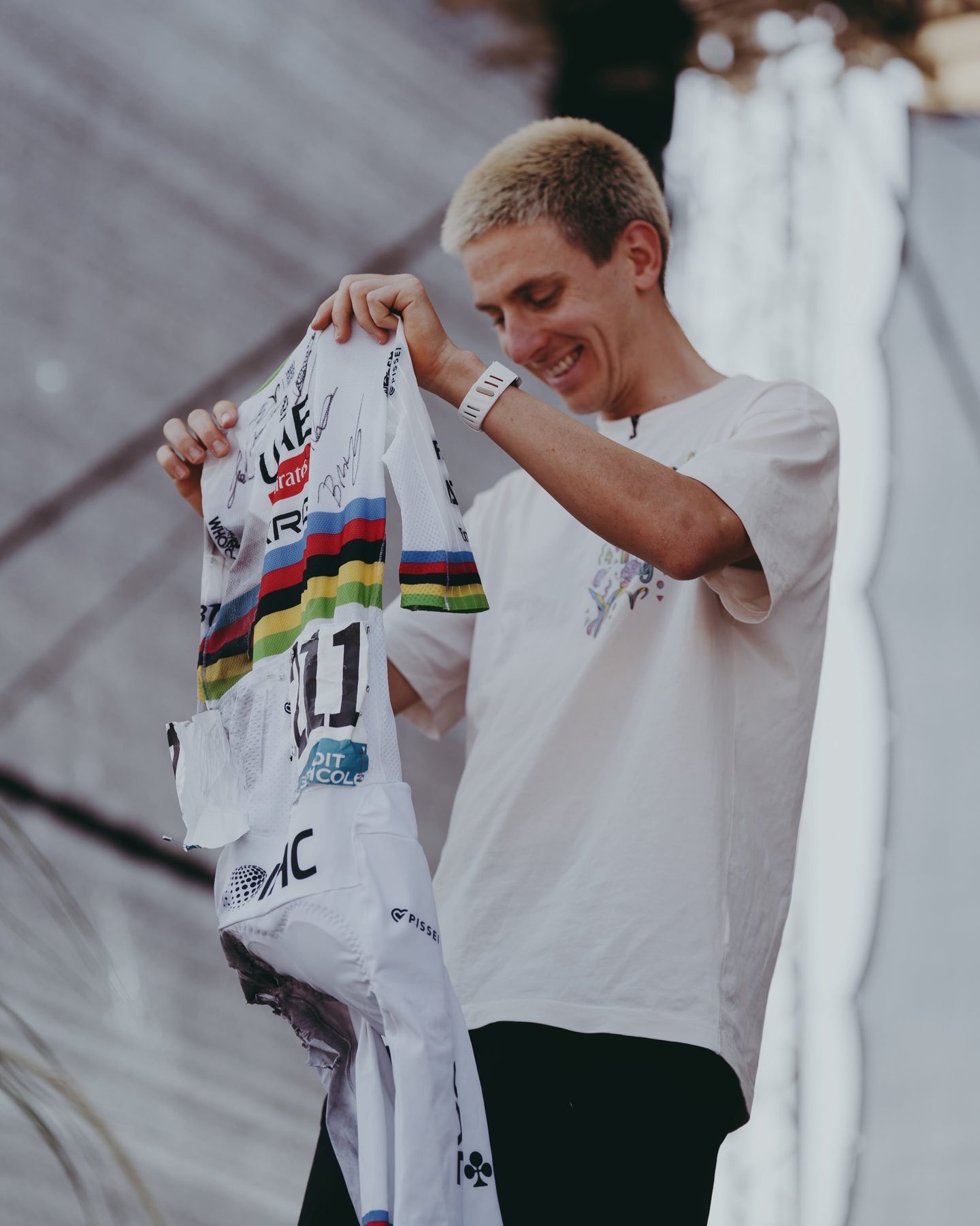 Tadej Pogačar smiling as he holds the signed jersey